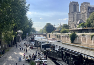 Notre-Dame de Paris et la péniche "Le Son de la Terre". Sur le quai et sur le pont du bateau, le public du Club des Mélomanes déguste un brunch le dimanche matin au concert de musique de chambre intitulé "Le Brunch des Mélomanes"