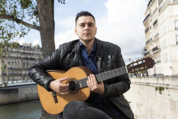 Sotiris Athanasiou jouant de la guitare sur les bords de la Seine à Paris.